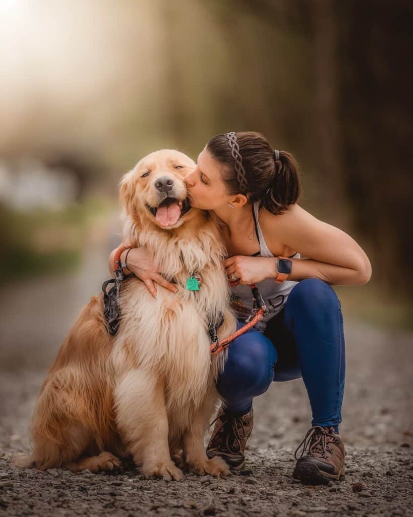 Woman kissing her happy and affectionate golden retriever on a hike